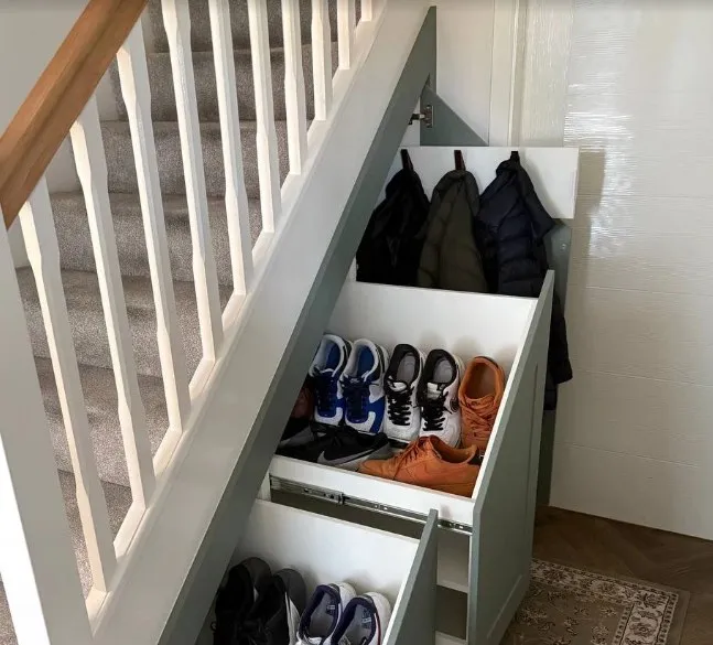 Coats on hooks behind an open sage door, with two shoe drawers pulled out below