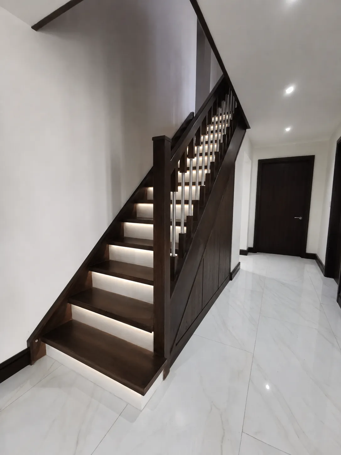 Dark walnut under stairs storage matching a walnut staircase with LED lit steps and marble floor