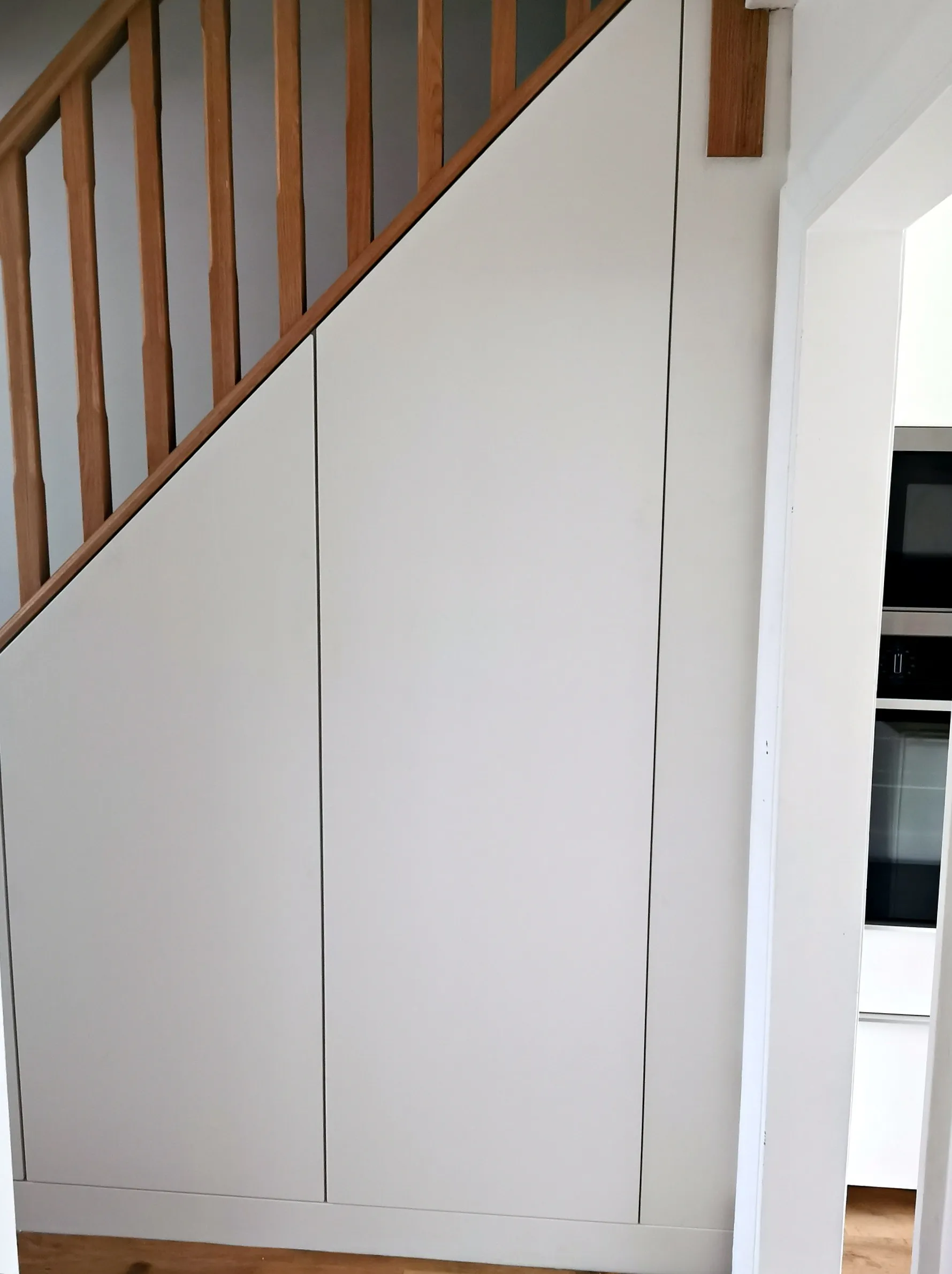 The same under stairs storage with white doors fitted, trims scribed to the wall and the run aligned