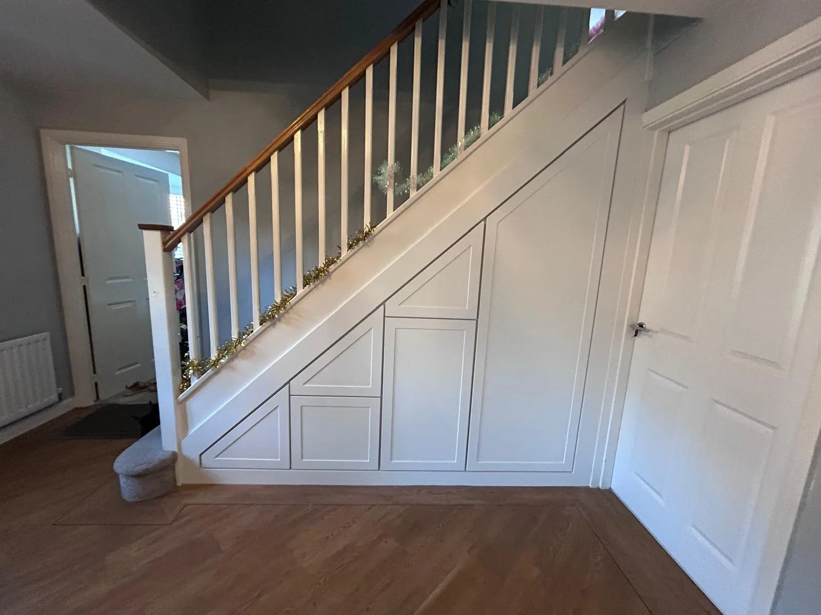 A white under stairs run of four panelled doors and drawers beside an oak and white balustrade