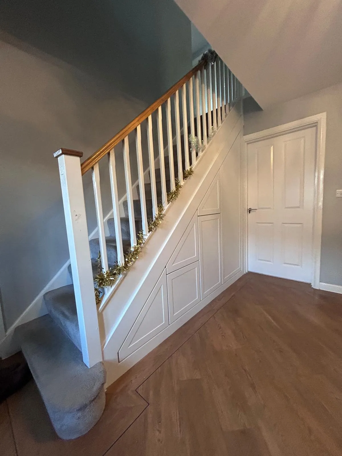 The white under stairs run seen from the stairs, with a tall cupboard beside a panelled door