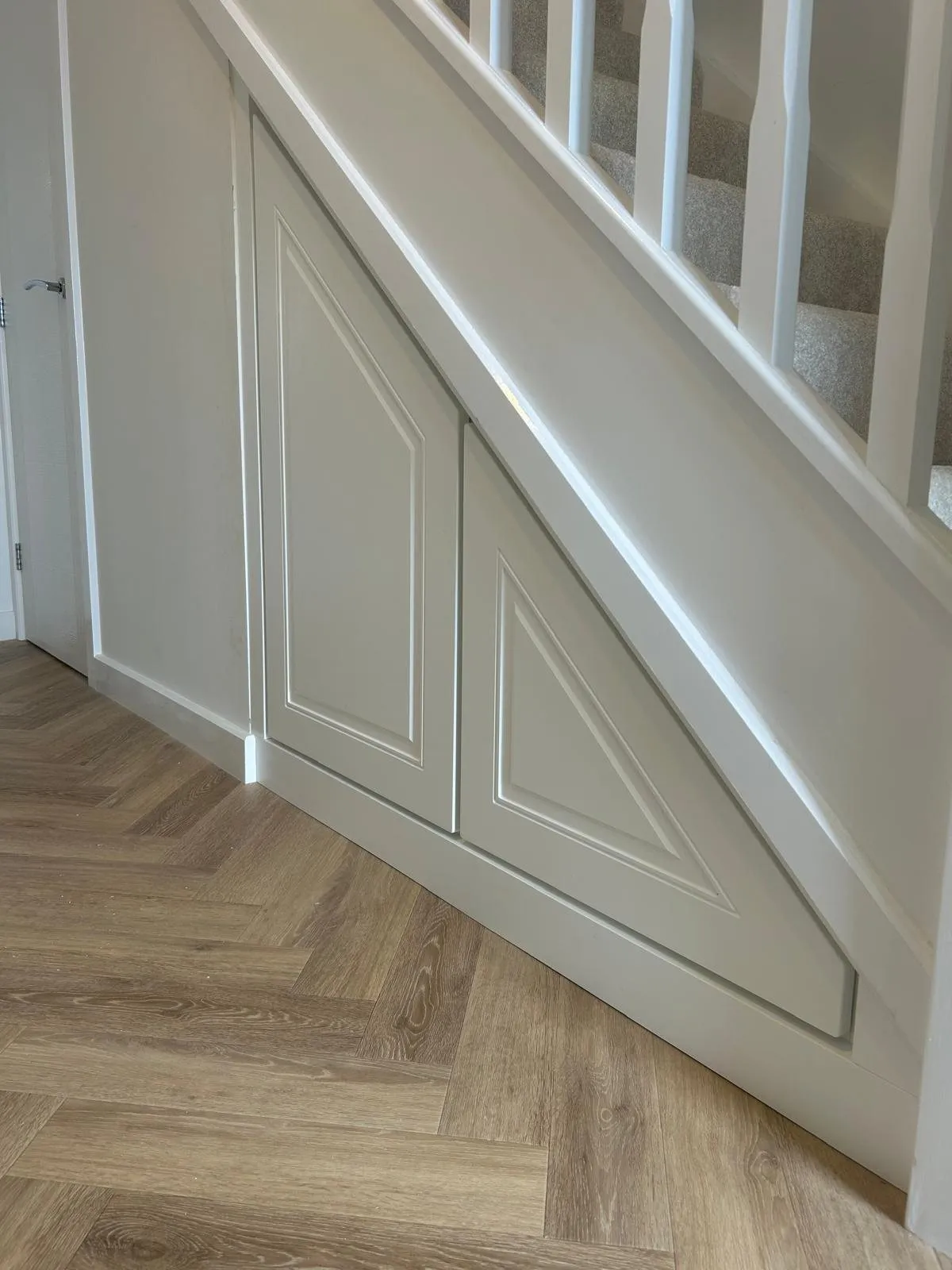 Two moulded panel doors under a white staircase on a herringbone floor