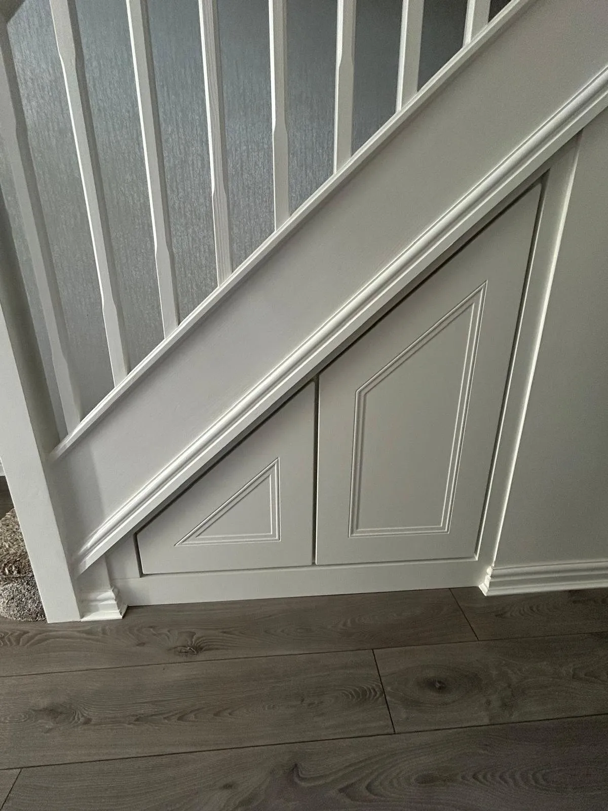 Two grey beaded panel doors under a white balustrade on grey wood flooring