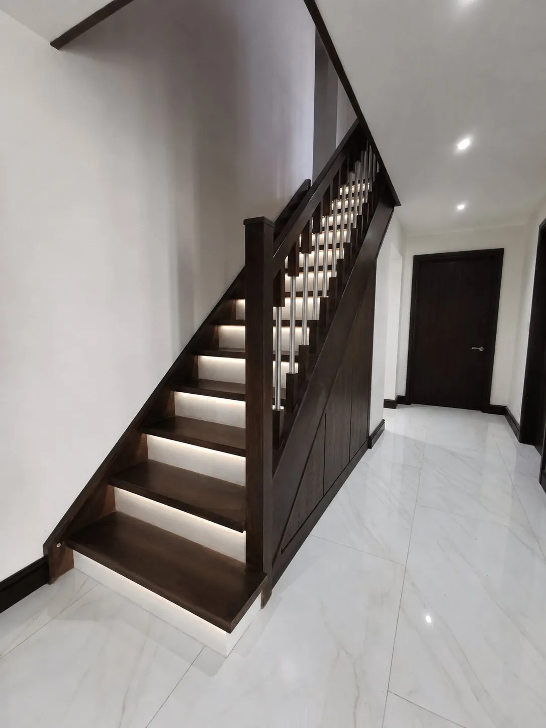 A dark walnut staircase with lit treads and matching walnut under stairs doors