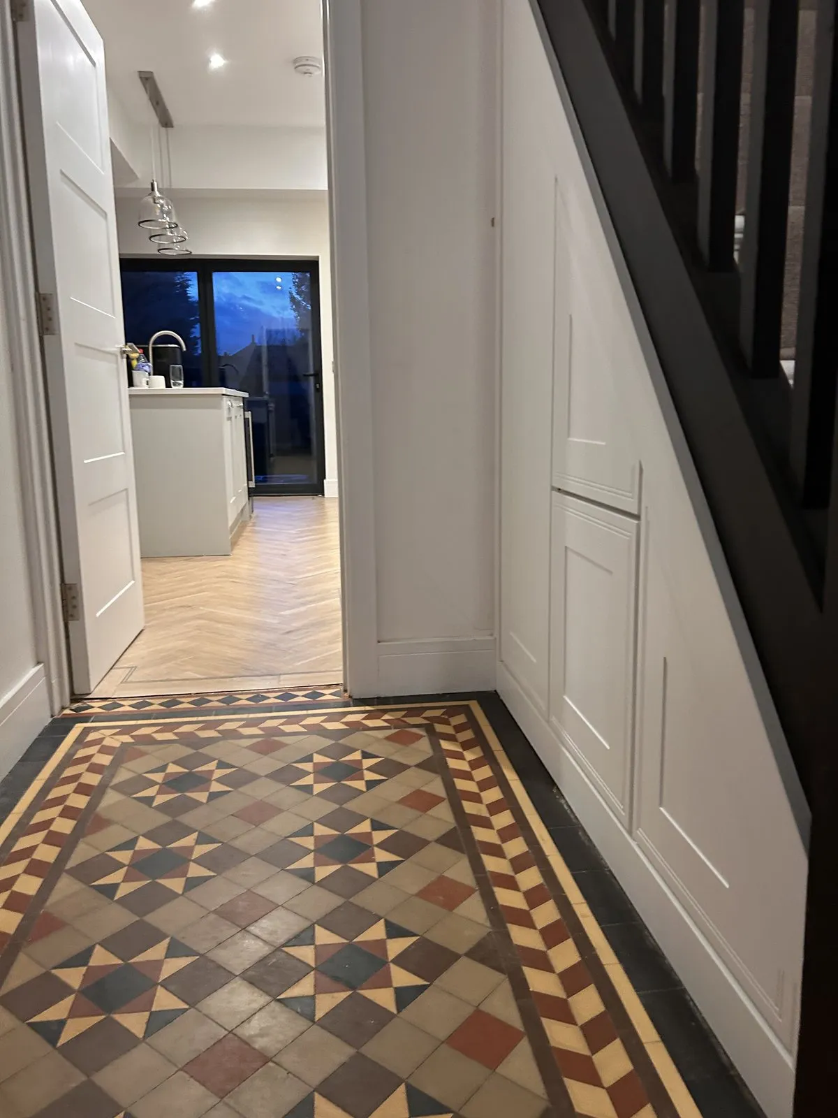 A tall white panelled cupboard under the stairs in a hallway with Victorian patterned tiles