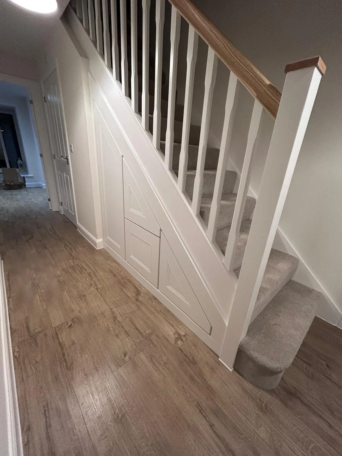 Two white doors and a drawer under a staircase with an oak handrail