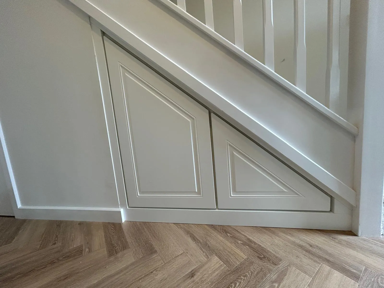 The same alcove fitted with two white panelled doors following the angle of the stairs