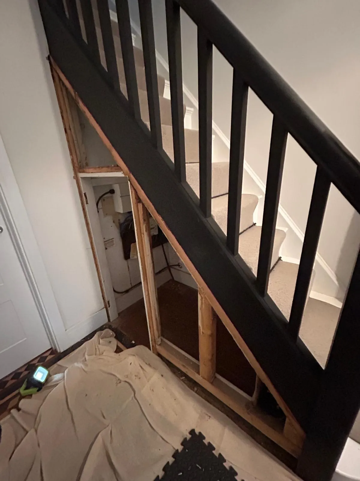 The under stairs space stripped back to its timber framing, with dust sheets protecting the tiled floor