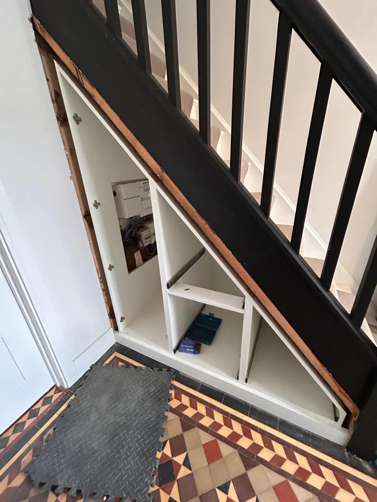 White carcasses fixed under the stairs with shelf bays and drawer runners, the electricity meter still accessible