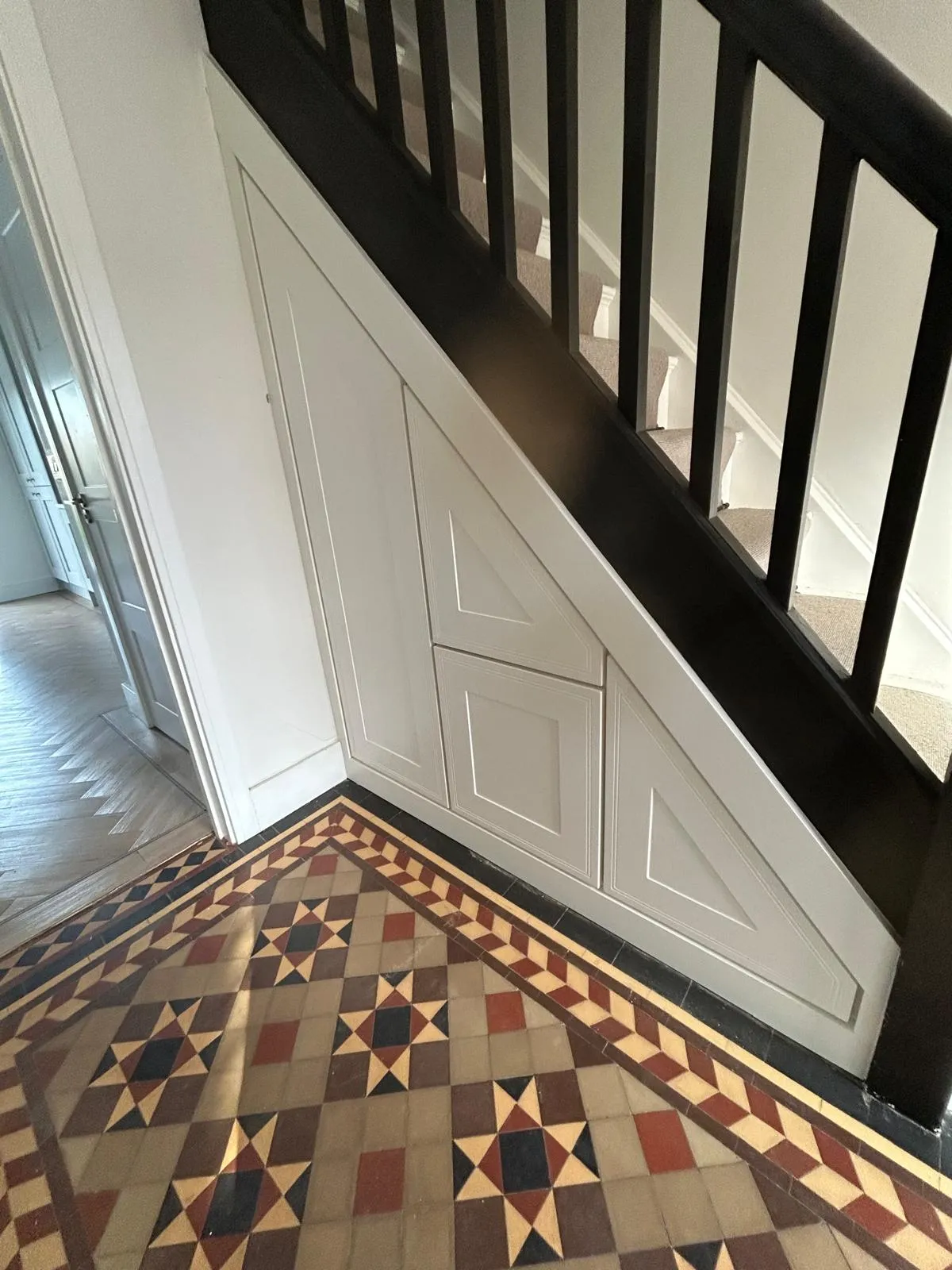 The finished white panelled under stairs storage with push to open fronts beside the Victorian tiled floor