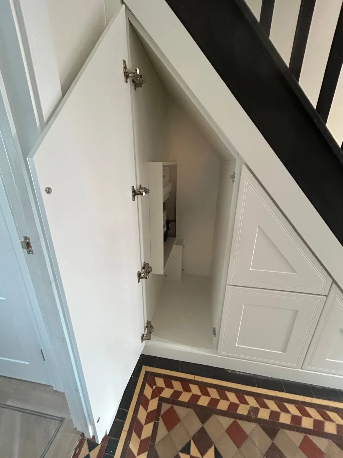 White under stairs cupboards in a period home with black staircase and Victorian tiled floor