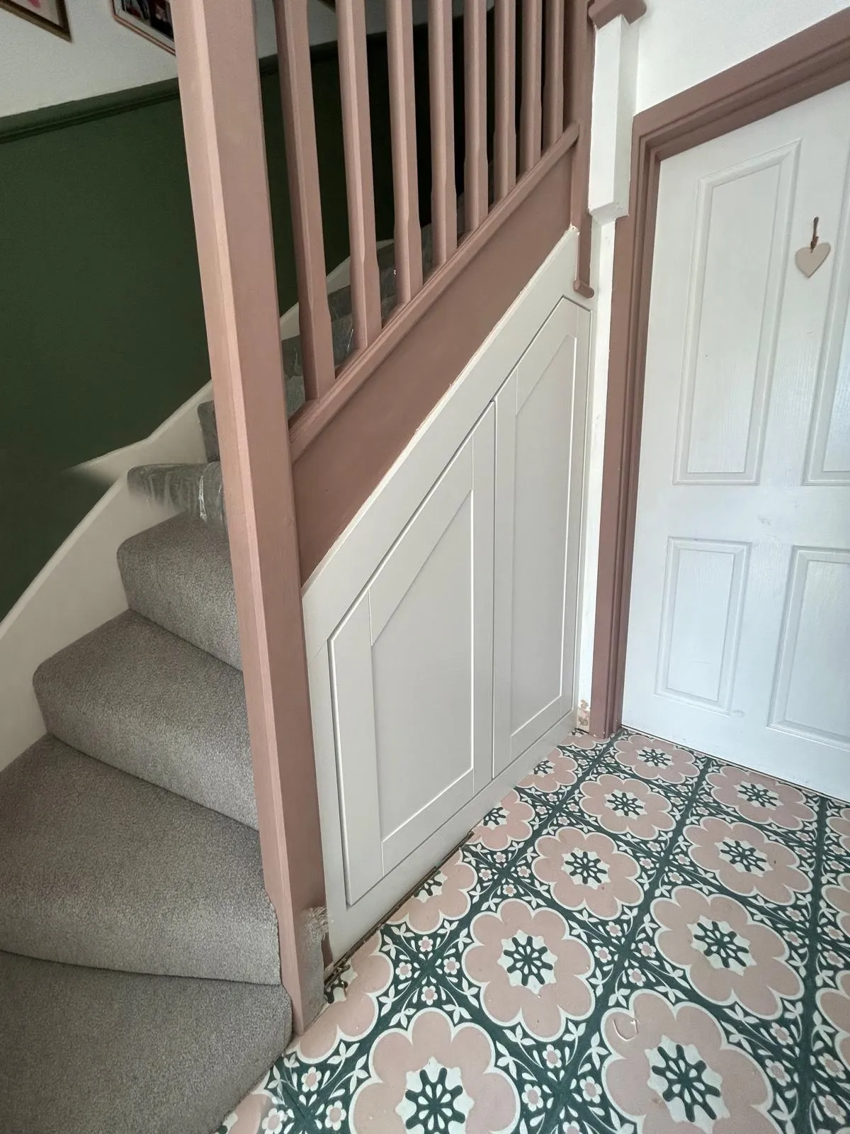 White Shaker under stairs doors, closed, beside a pink painted period staircase and patterned tiled floor