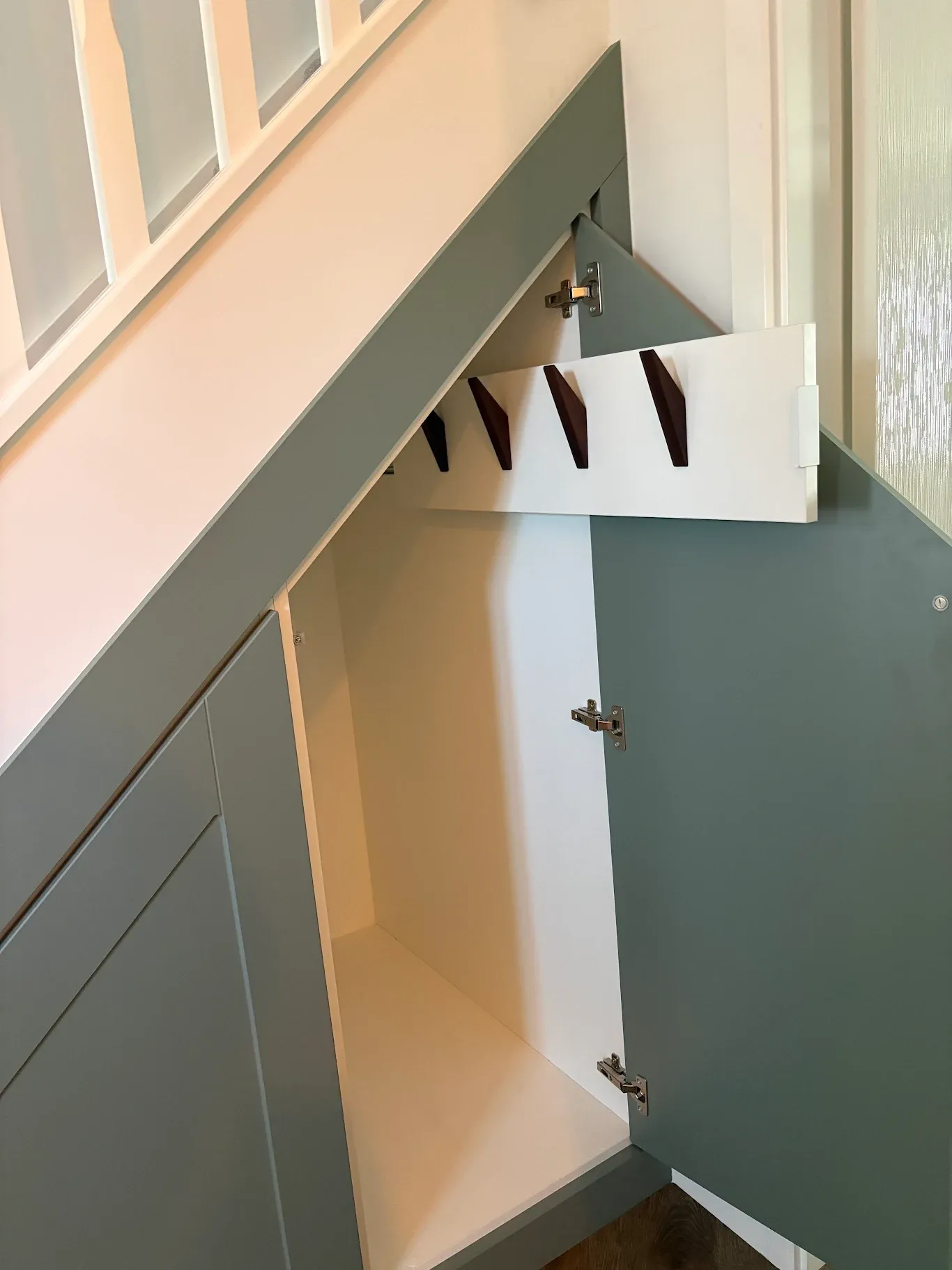 Sage green cupboard open with pull out coat hooks on walnut pegs