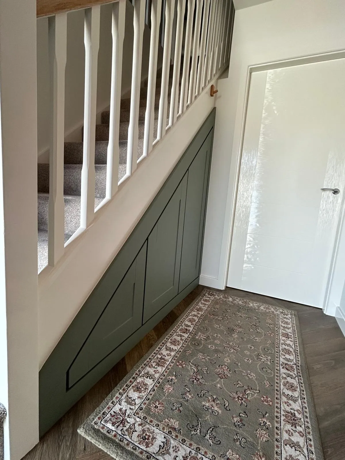 Sage green Shaker under stairs storage with three angled doors beside a white staircase