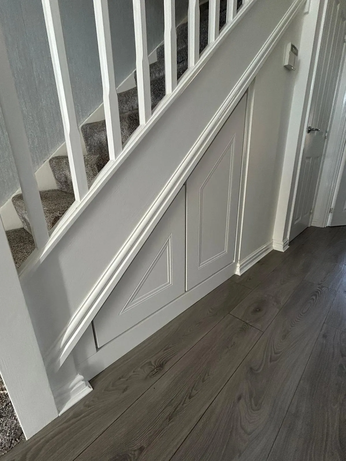 White panelled angled under stairs doors on grey wood flooring