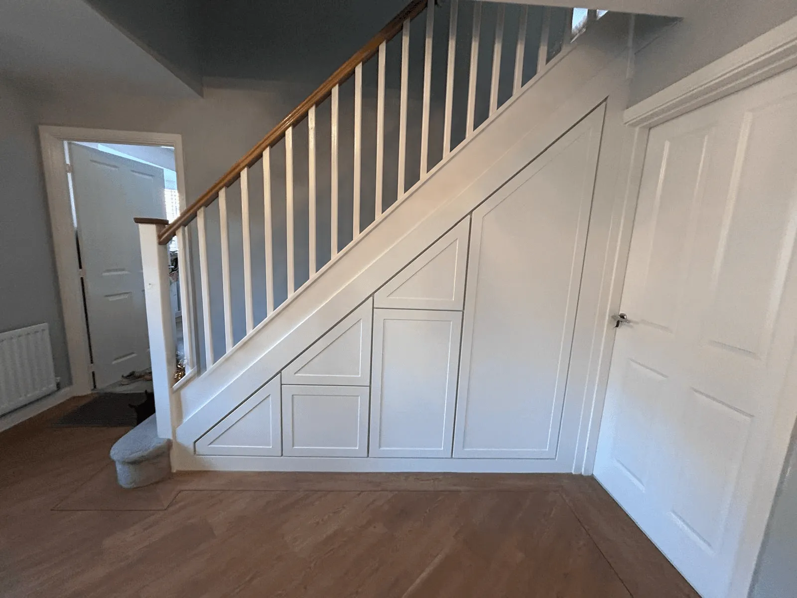 Full width under stairs storage run with four white Shaker style doors stepping down beneath a turned staircase